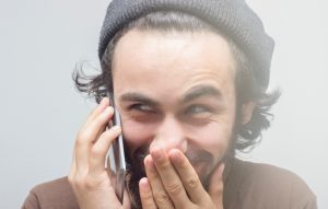 Smirking young man talking on phone over gray background